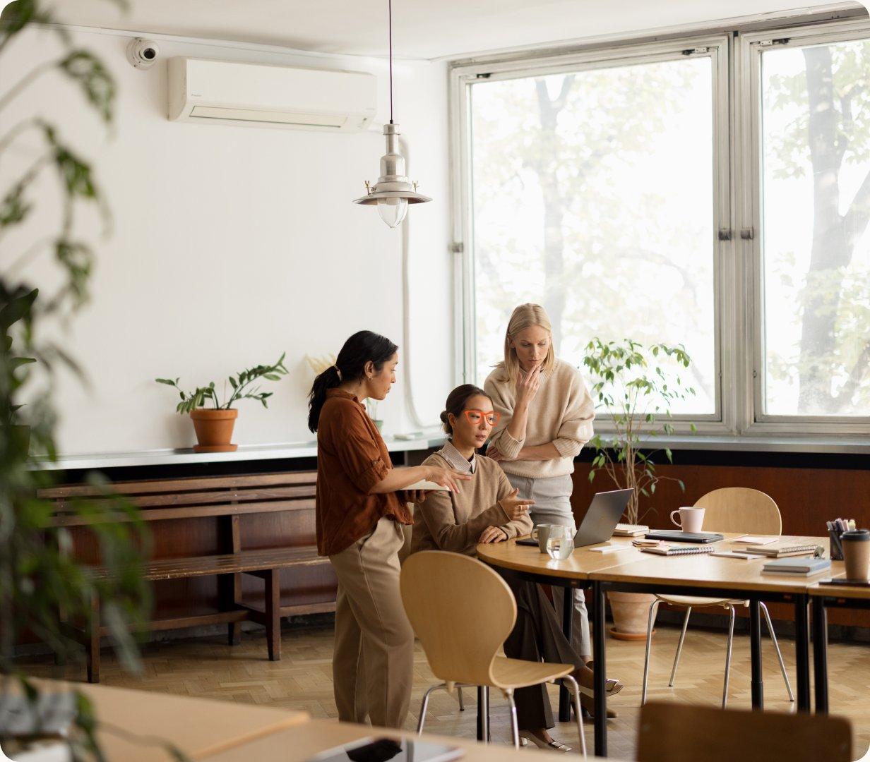 Three colleagues reviewing a laptop together in a bright office