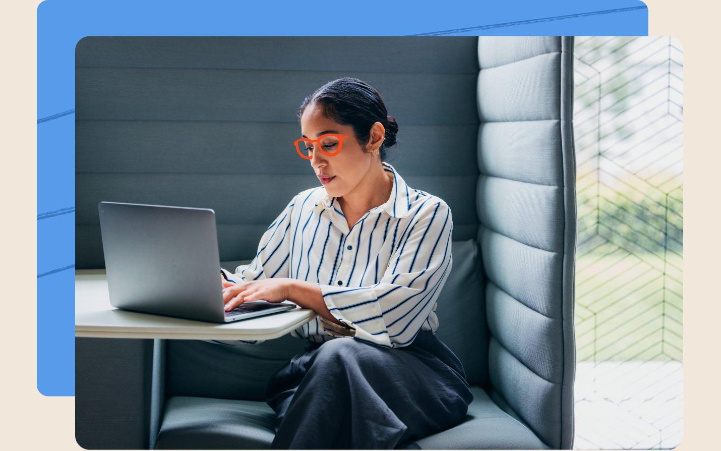 Person working on a laptop in an office booth, framed by a blue panel