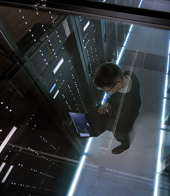 Male data manager holding laptop standing in data center